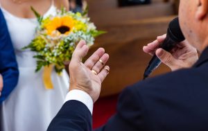 Wedding officiant holding wedding rings in front of a bride and groom