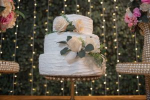 Tiered wedding cake on a stand sitting on a table with flowers either side