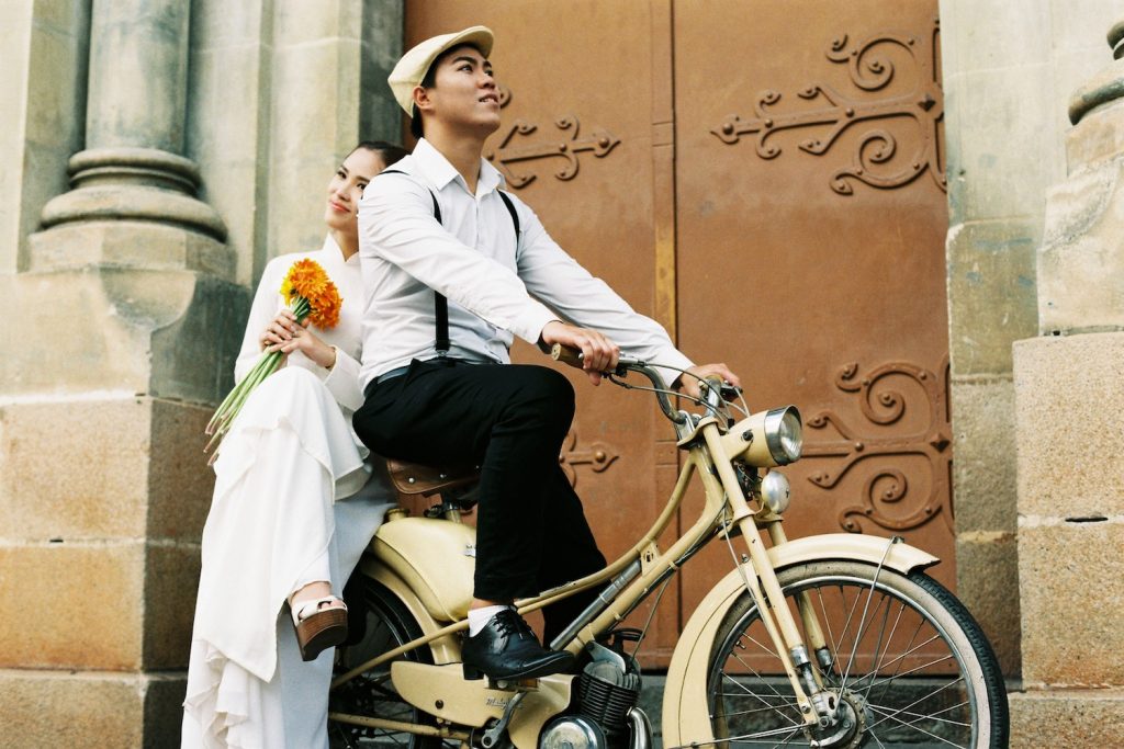 Bride and groom standing in front of ornate doors on a bicycle
