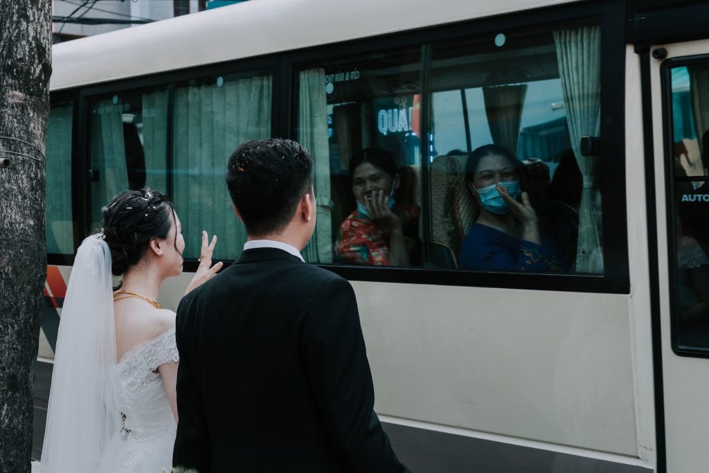Bride and groom waving at their guests on a bus