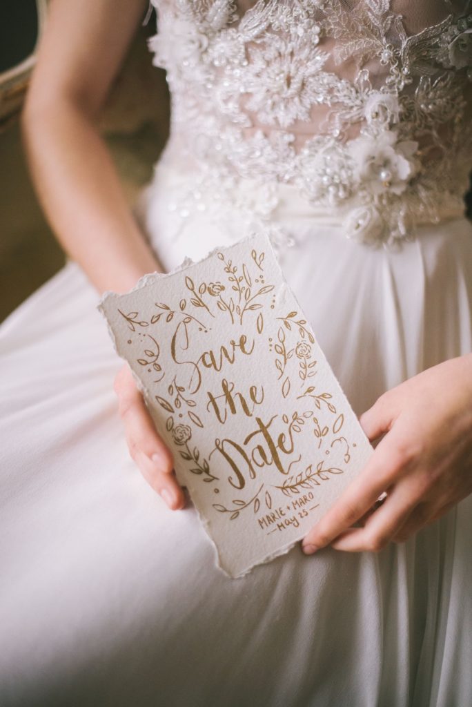 Bride in her wedding dress standing holding a Save the Date for the wedding