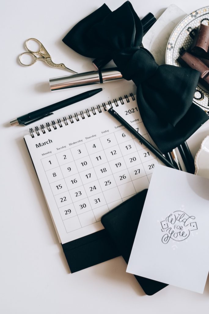 Wedding Day Timeline with calendar and bow-tie and other stationery items on a white surface