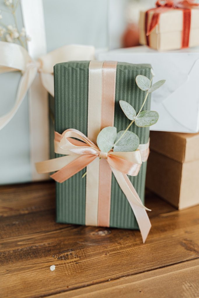 Present wrapped in green paper with pink ribbons and small plant as decoration